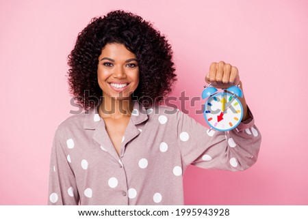 Photo of pretty charming curly dark skin woman dotted nightwear holding blue bell isolated pink color background