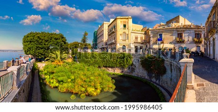 The Fountain of Arethusa and Siracusa (Syracuse) in a sunny summer day. Sicily, Italy. The Fountain of Arethusa in Ortygia, historical centre of Syracuse, Sicily, Italy. Royalty-Free Stock Photo #1995986405