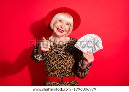 Photo of aged woman happy positive smile hold cash dollars rich indicate finger you isolated over red color background