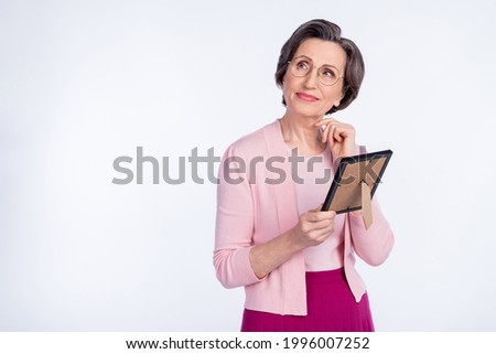 Photo of dreamy cute age woman dressed pink outfit spectacles holding photo frame looking empty space isolated white color background
