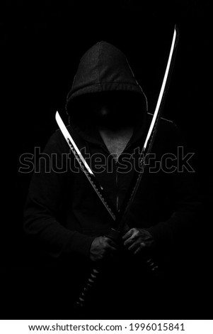 A fighter in black clothes with a hood on his head holds two sparkling Japanese swords on a black background