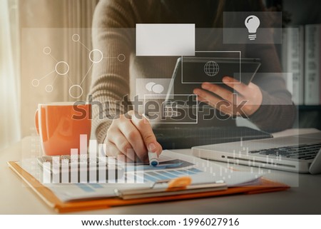 Female businessman hand working at a tablet computer and writing on a notepad with a pen in the office on the wooden desk there a graph business diagram.