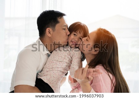 Portrait of attractive asian dad and mom kissing daughter's cheek together close up on isolated white studio background. Parenthood and childhood lifestyle or love and bonding in soft tone concept.