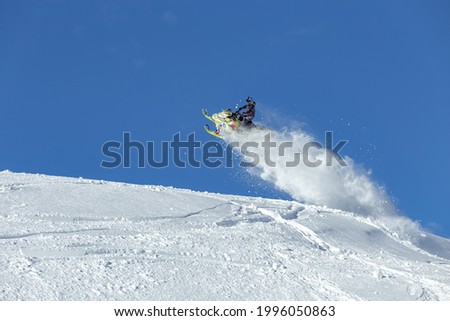 the guy is flying and jumping on a snowmobile on a blue background leaving a trail of splashes of white snow. bright snowmobile and suit without brands. extra high quality Royalty-Free Stock Photo #1996050863