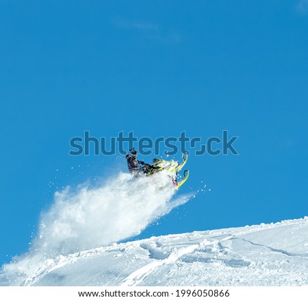 the guy is flying and jumping on a snowmobile on a blue background leaving a trail of splashes of white snow. bright snowmobile and suit without brands. extra high quality Royalty-Free Stock Photo #1996050866