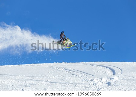 the guy is flying and jumping on a snowmobile on a blue background leaving a trail of splashes of white snow. bright snowmobile and suit without brands. extra high quality Royalty-Free Stock Photo #1996050869