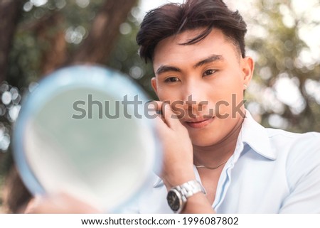 A vain young man checks his reflection in the mirror. Narcissistic behavior. Royalty-Free Stock Photo #1996087802