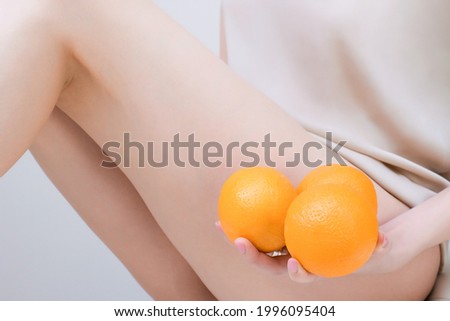 young woman is holding an orange on a light background. Cellulite problem concept