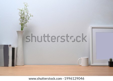 Modern workplace with white picture frame, books and coffee cup on wooden table.