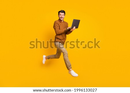 Full size profile photo of impressed nice brunet man hold laptop wear sweater isolated on yellow background