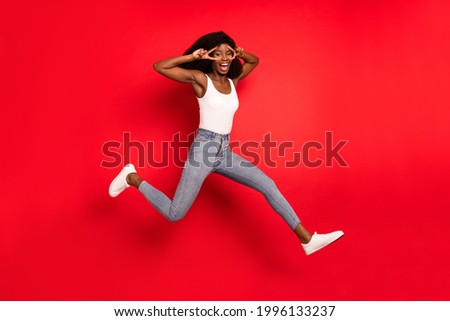 Full length photo of young afro girl happy positive smile jump up show peace cool v-sign isolated over red color background