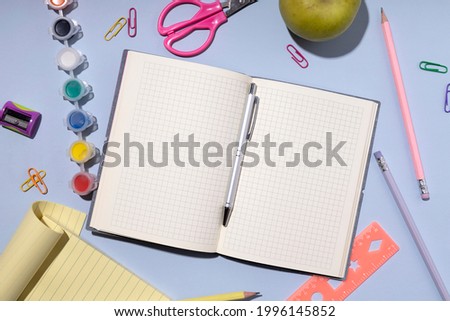 Top view of checkered notebook,ruler,pencils,paints,scissors and other stationary on the blue table.Empty space