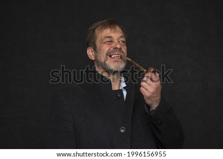 Portrait of an elderly man 45-50 years old with a gray beard in a black coat, smoking a pipe on a dark background.Concept: retired military man, writer or sailor.