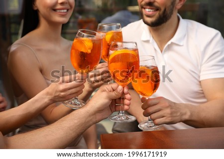 Friends clinking glasses of Aperol spritz cocktails outdoors, closeup Royalty-Free Stock Photo #1996171919