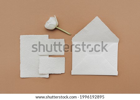 Still life scene with white tulip flower and blank business, greeting card, invitation mockup on brown background. Flat lay, top view.
