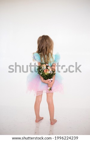 a little girl in a festive dress with a tutu skirt stands with her back and holds a bouquet of fresh flowers on a white background with a place for text