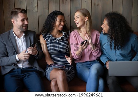 Happy young mixed race friendly people using different gadgets, sharing funny photo or video content in social networks, having fun playing games, millennial generation and tech addiction concept.