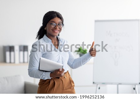 Psychology teacher or business coach giving seminar or presentation, showing thumb up gesture at office. Black female lecturer recommending training course on personal growth and motivation Royalty-Free Stock Photo #1996252136