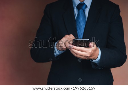 Businessman using a smartphone while standing with a brown background. Space for text. Communication and technology concept.