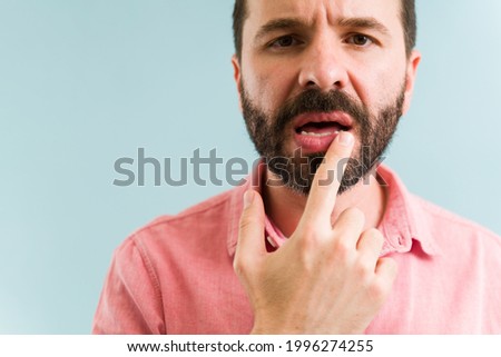Attractive man touching his mouth and feeling a little pain because of his dry lips. Close up of a latin man applying lip balm Royalty-Free Stock Photo #1996274255