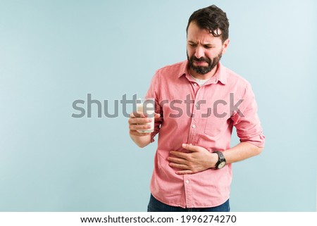I don't like milk. Upset man trying to drink a glass of milk. Sick man with lactose intolerance consuming dairy products Royalty-Free Stock Photo #1996274270