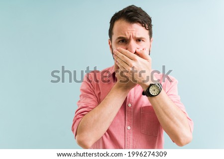 Hispanic man feeling ashamed because of his halitosis. Handsome young man in his 30s covering his mouth due to bad breath Royalty-Free Stock Photo #1996274309