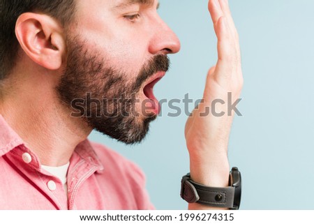 Close up of a good-looking man putting his hand in front of his mouth and checking his bad breath before a date Royalty-Free Stock Photo #1996274315