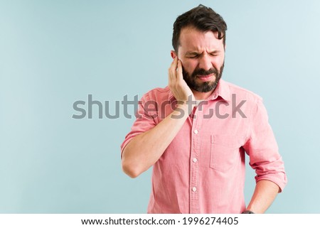 Worried man in his 30s aching and listening to a ringing in his ear. Pained man with touching his ears because of an infection  Royalty-Free Stock Photo #1996274405