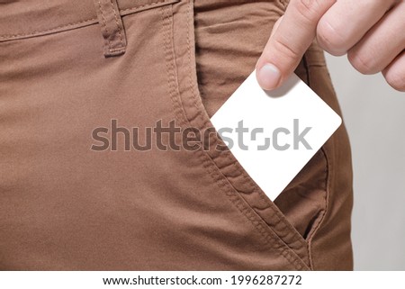 Close up of male hand taking out blank white card from side pocket of brown pants, copy space.
