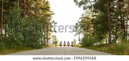 Company of young people riding in row on scooter motorbikes along asphalt road in sunny nature, panorama. Leisure, fun and entertainment concept Royalty-Free Stock Photo #1996299368