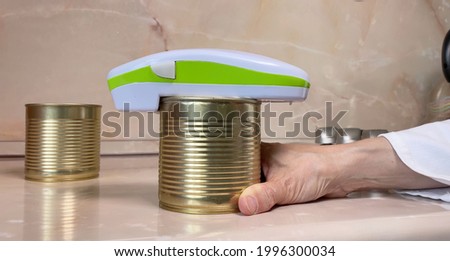 Electric can opener and canned goods on kitchen table Royalty-Free Stock Photo #1996300034