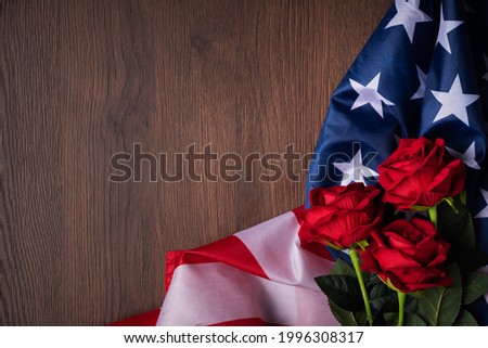 Concept of U.S. Independence day or Memorial day. National flag and red rose over dark wooden table background.