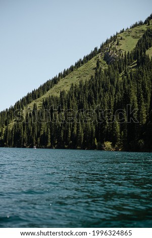 Picture of lake and green peak of the mountain. Boat on the water. Blue lake in the summer