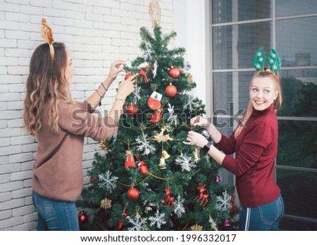 The attractive cheerful female friend decorates the Christmas tree in preparation for the celebration of Christmas and New Year. vintage tone