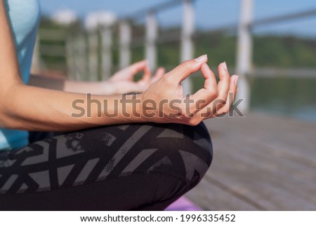Close-up of hands of a young sporty woman who meditates while holding fingers in yoga sign sitting on the sea pier. Peaceful girl keeps hands in mudra gesture sitting in the lotus pose