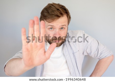 Calm, confident man makes a stop gesture, palm forward and looks seriously into the camera. 
