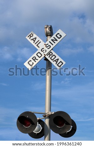 Post mounted railroad crossing sign and signal lights against a lightly cloudy blue sky.