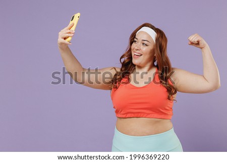 Young chubby overweight plus size big fat fit woman in red top warm up training hold yoga mat do selfie shot on mobile phone show muscles isolated on purple background home gym Workout sport concept