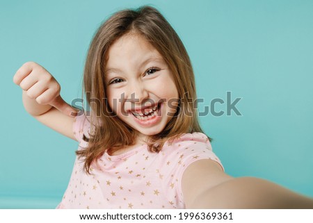 Closeup little fun kid girl 5-6 years old wears pink dress doing selfie shot on mobile phone isolated on pastel blue color background child studio portrait. Mother's Day love family lifestyle concept