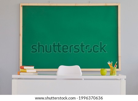 Back To School background with a clean green school board. Indoor shot of a teacher's desk and a copy space blackboard in a modern school classroom. Education concept