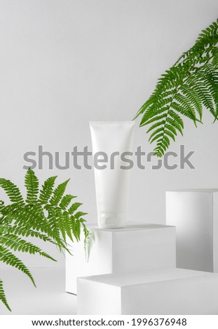 White bottle cosmetic product on white platform with fern leafs. Exhibition white podium with cosmetic product. Blank package mockup, commercial showcase.