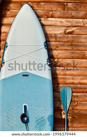 SUP board and surfboard with paddle on wooden wall background close up. Surfing and sup boarding equipment in sunset lights close-up. Outdoor water sports. Surfing lifestyle backgrounds.