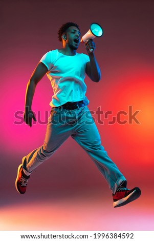 Image of young positive african man hovered in the air walking, jumping shouting in loudspeaker on bright colorful neon studio background.