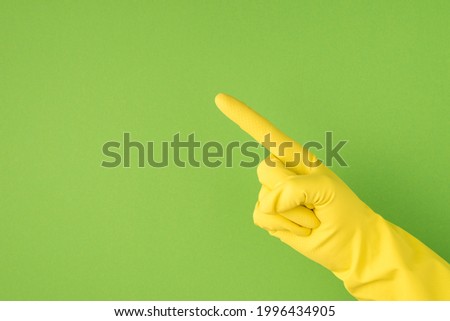 Above photo of hands in yellow gloves making the gesture as directing with index finger isolated on the green background