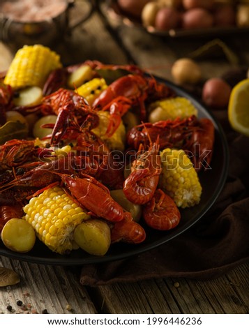 In the photo, a black dish with boiled crayfish and pieces of corn. On the right you can see a slice of lemon and vegetables. Close-up, macro photography. Careful viewing.