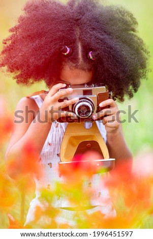 Childhood and explorer concept - A small curly haired African American girl holding a flower camera.