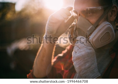 A man in goggles, gloves and a respirator. Means of protection. Young worker removes or puts on protective equipment during dusty and dirty work Royalty-Free Stock Photo #1996466708