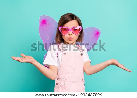 Photo of impressed puzzled schoolgirl dressed pink overall eyewear wings shrugging shoulders isolated turquoise color background