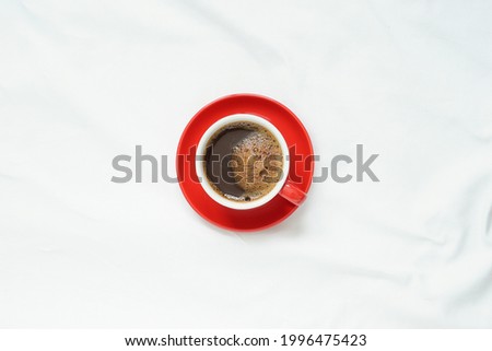 top view of hot coffee in red ceramic cup on red ceramic plate placed on blank clean tablecloths with soft light in the morning Royalty-Free Stock Photo #1996475423
