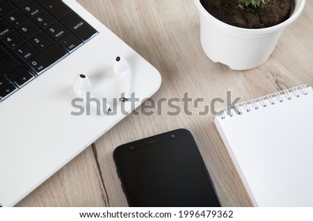 Smartphone, wireless earphones,  notebook and accessories on wooden background.
